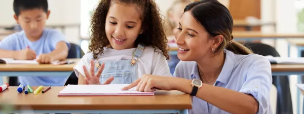 Female teacher teaching a young girl at her desk in the classroom