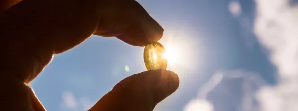 Hand holding up Vitamin D3 pill in sunlight