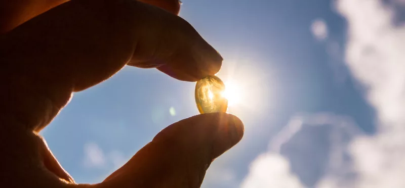 Hand holding up Vitamin D3 pill in sunlight
